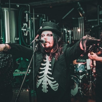 A man in a skeleton costume singing into a microphone releasing the double single "Virginia Plain/April" by The Antoine Poncelet Band.