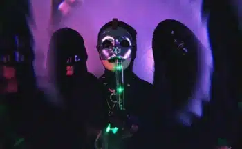 A group of people in black masks standing in front of a purple light.