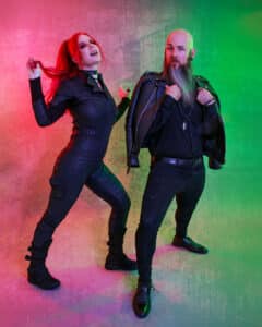 Two people in black outfits posing in front of a colorful background.