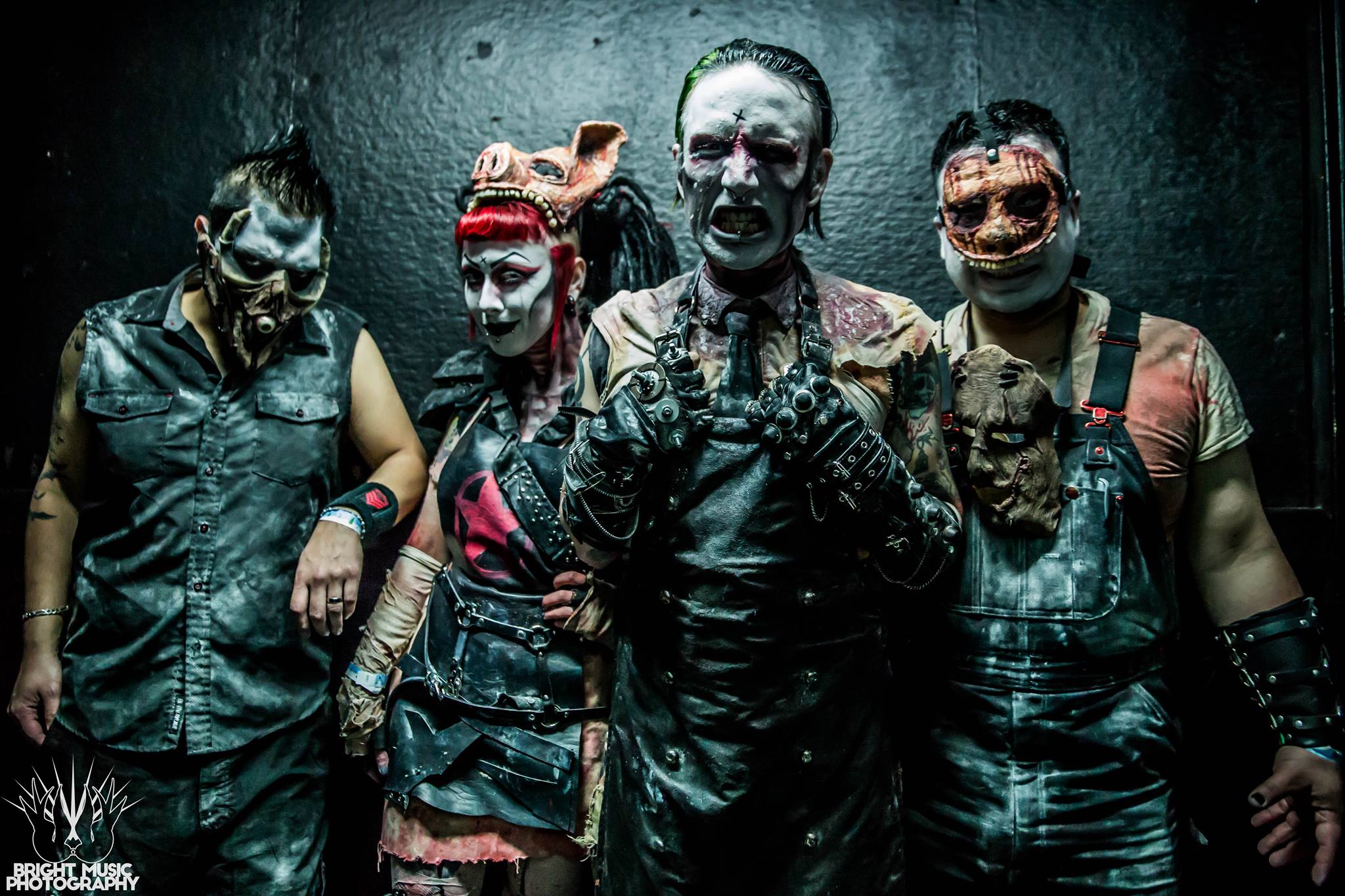 Four people in detailed horror-themed costumes and makeup stand against a dark background, embodying the chilling essence of Dead Animal Assembly Plant. It's as if Zach is guiding an eerie interview through their haunting visuals.